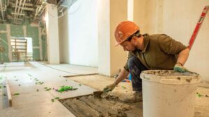 Construction worker laying bathroom floor tiles during renovation