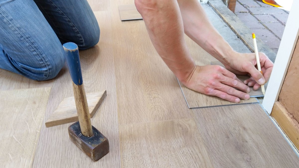 Craftsman measuring and marking wooden floor panels for precise installation